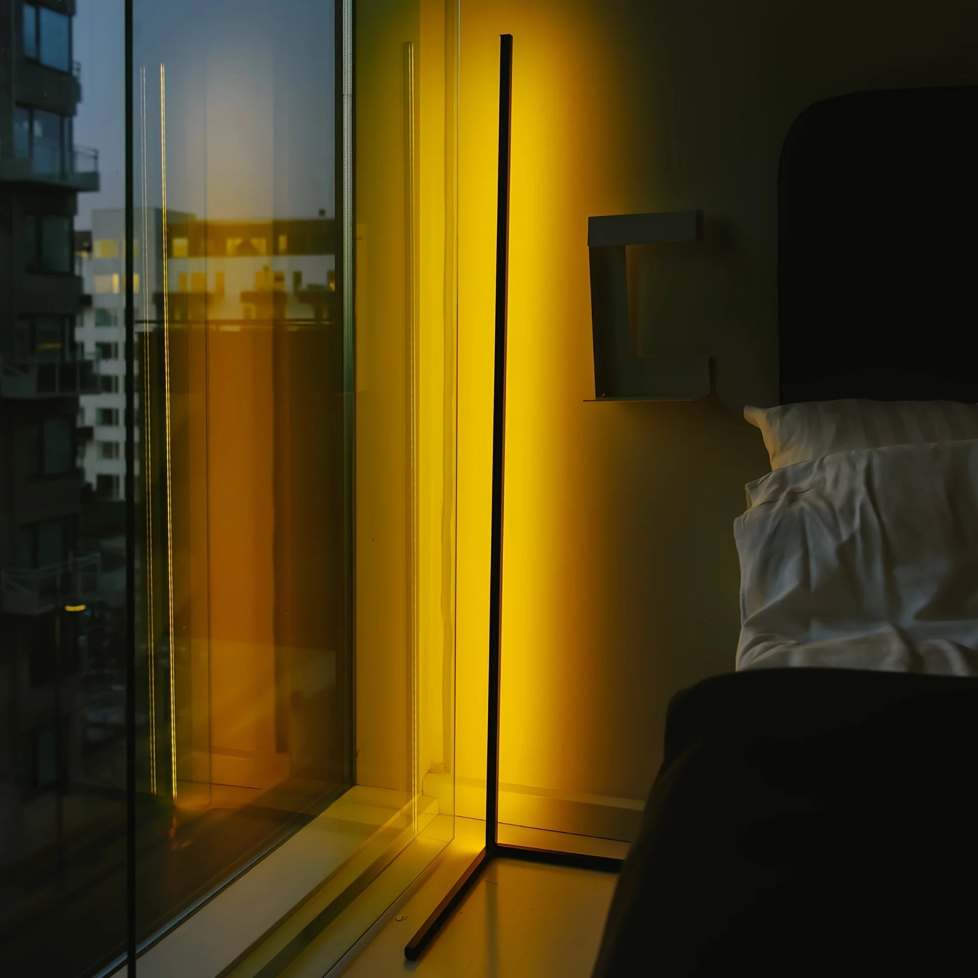 Modern bedroom with a floor lamp casting a warm glow near a window with cityscape view.